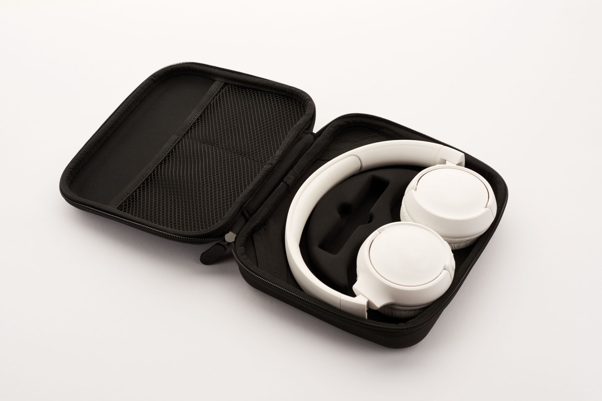 White wireless headphones neatly packed in a black portable travel case on a neutral background.