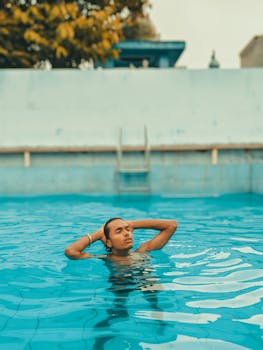 Young man with long hair relaxing in a swimming pool, enjoying summer outdoors.