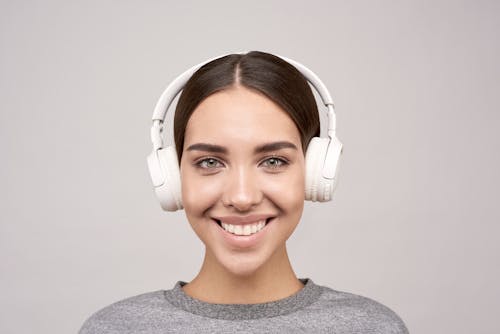 Woman Wearing Gray Crew-neck Shirt Using White Wireless Headphones Smiling