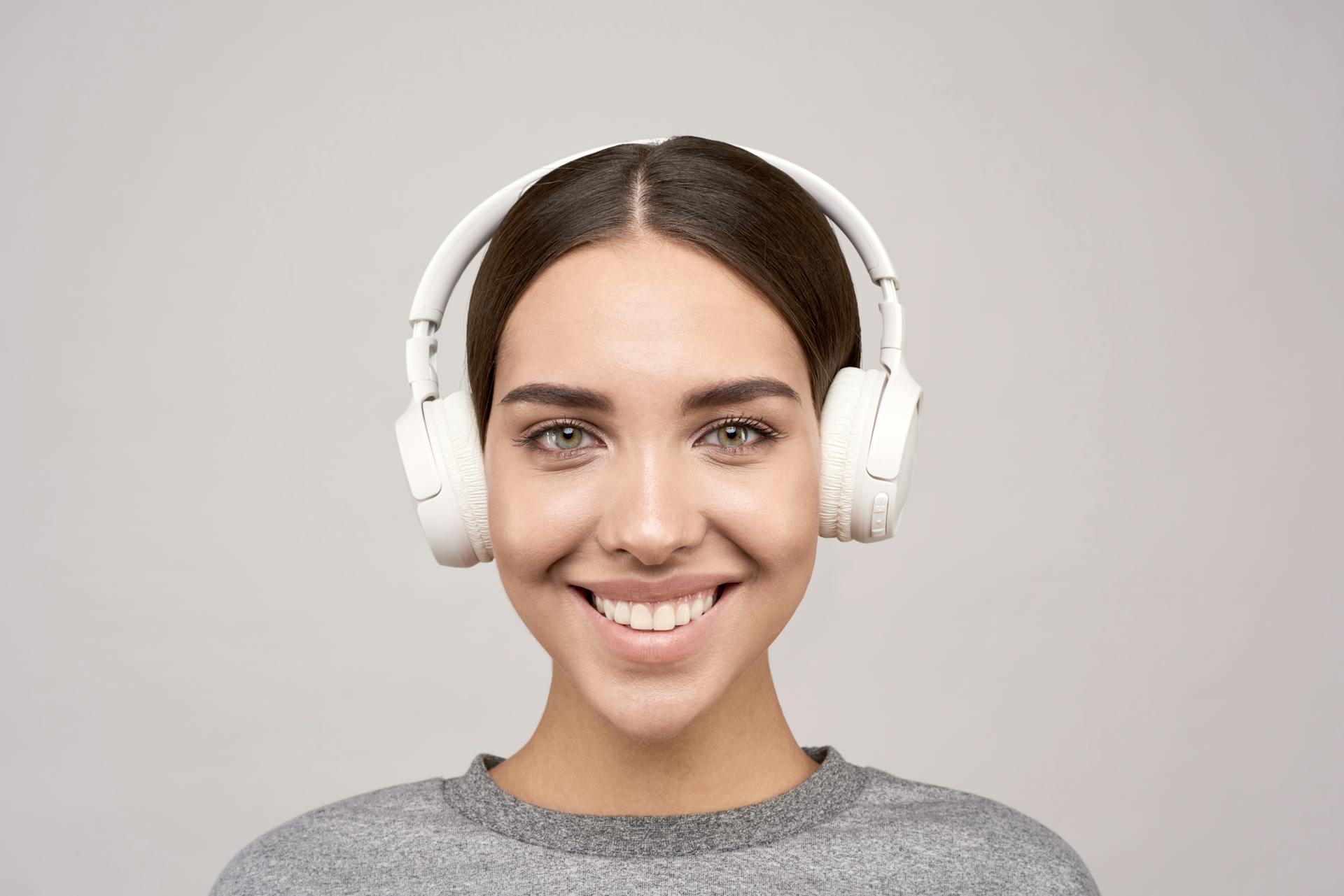 Portrait of a smiling woman wearing white headphones, enjoying music indoors.