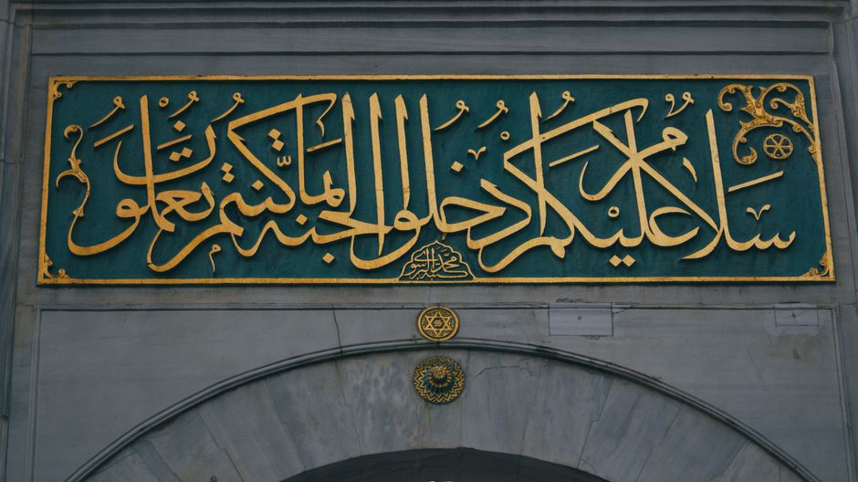 Elegant Arabic calligraphy sign adorns a historic stone arch with golden script and detailed design.