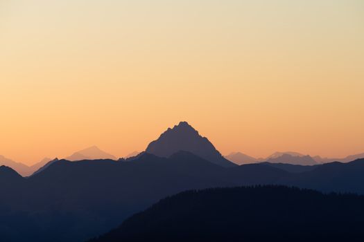 Serene mountain silhouette against a pastel orange sky during sunrise, capturing tranquility and nature's beauty.