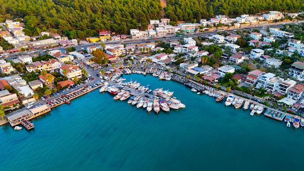 Aerial view of a picturesque coastal town harbor with boats docked, surrounded by lush greenery and colorful buildings.