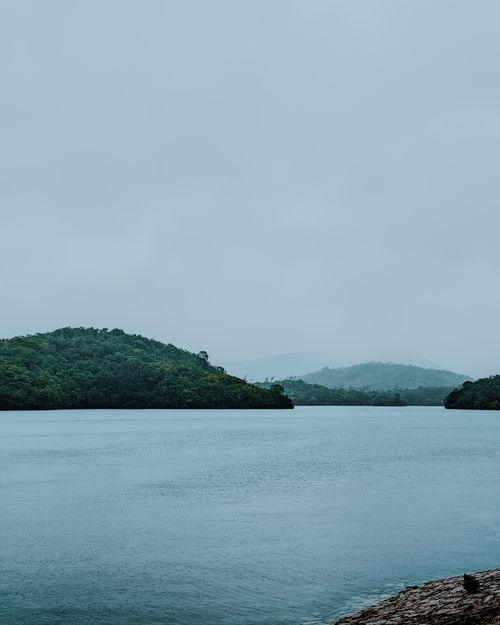 Free Peaceful view of Kerala backwaters surrounded by lush greenery and rolling hills during a cloudy day. Stock Photo