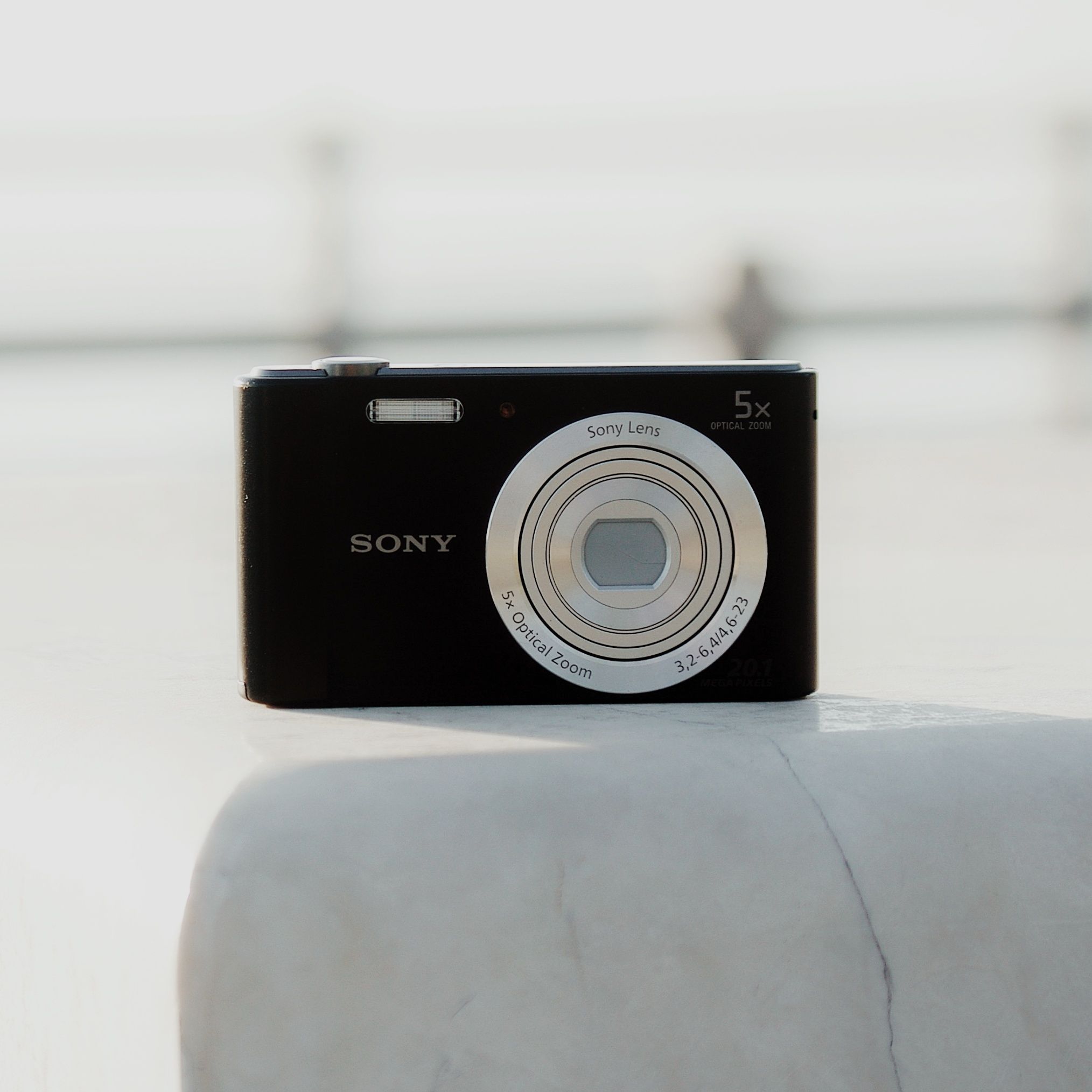 Close-up of a black digital camera with optical zoom lens displayed on a white surface outdoors.