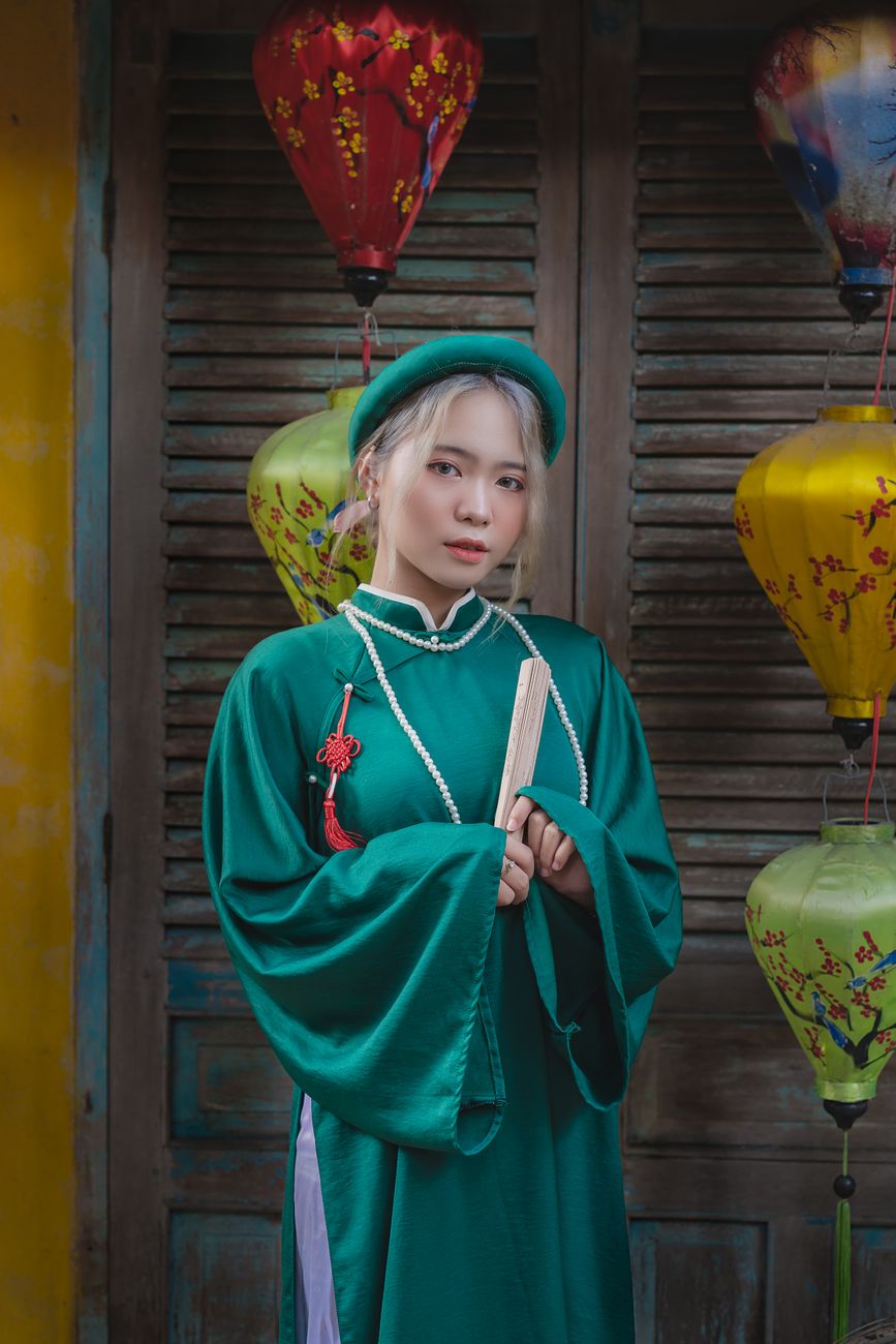 Woman in traditional Vietnamese dress holds a book surrounded by lanterns.