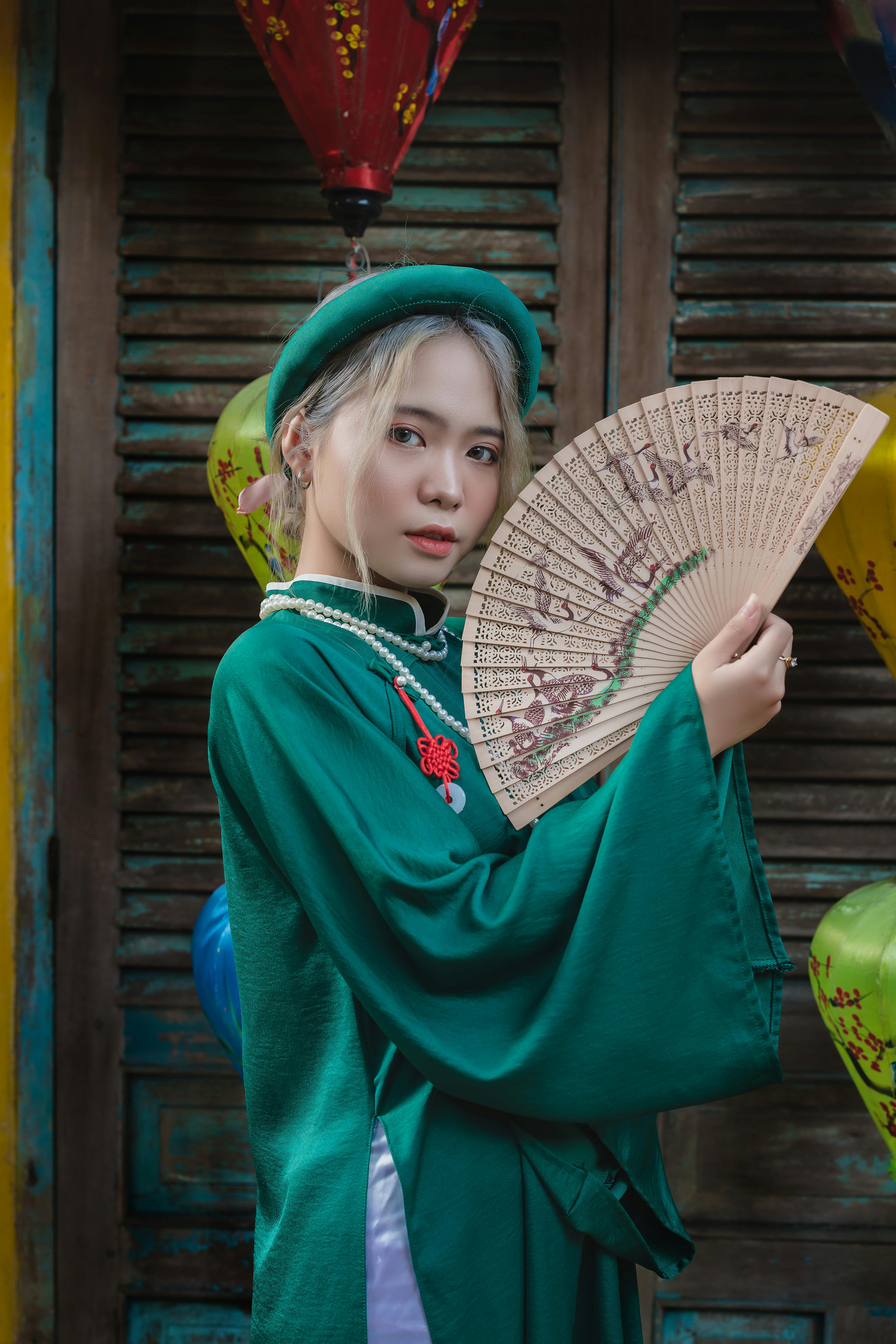 Elegant portrait of a woman in green traditional attire holding a decorative fan.