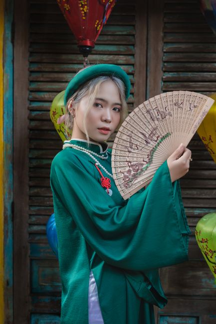 Elegant portrait of a woman in green traditional attire holding a decorative fan.
