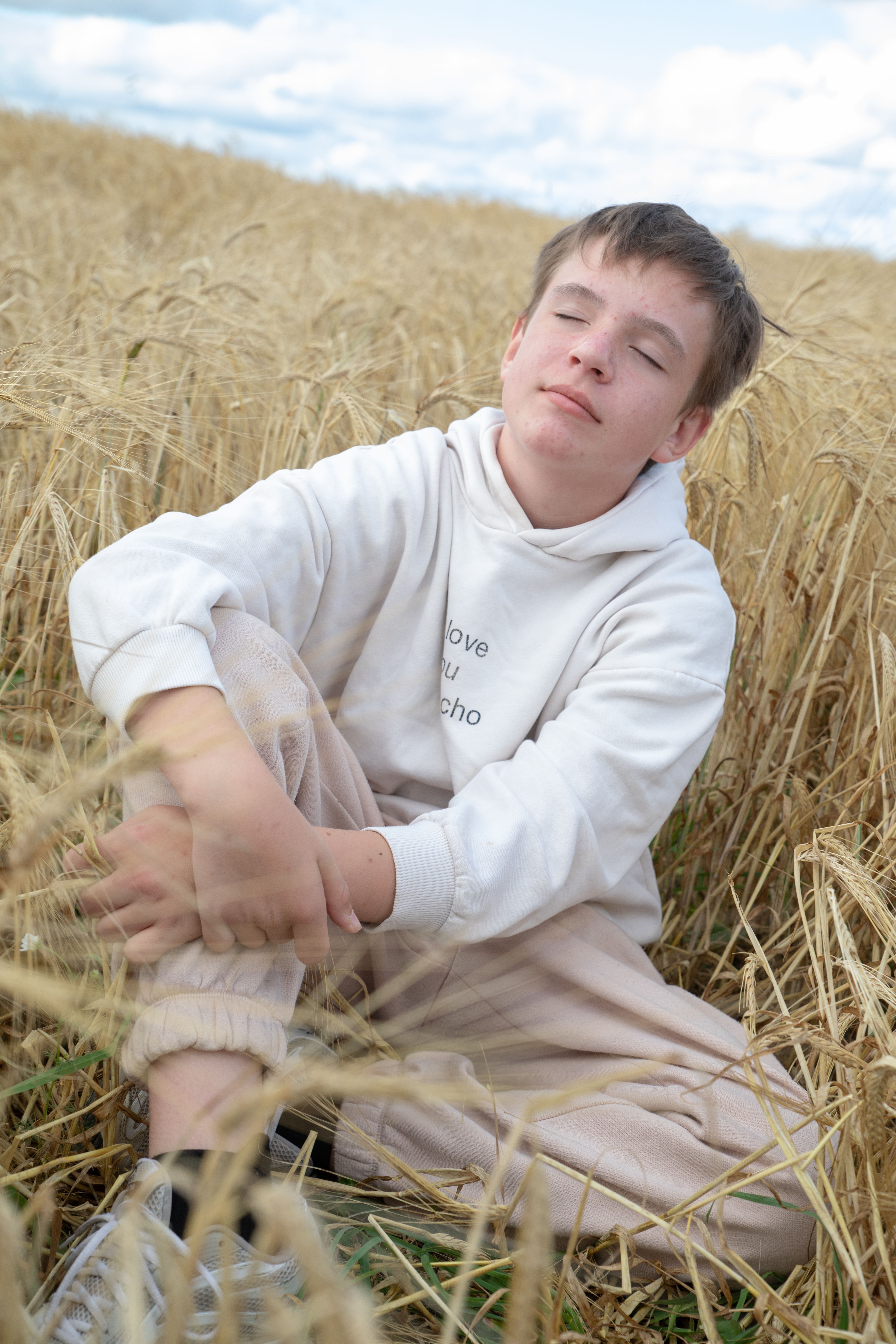 Fotomural Un adolescente disfruta de un momento de paz en un campo de trigo bajo un cielo azul claro.