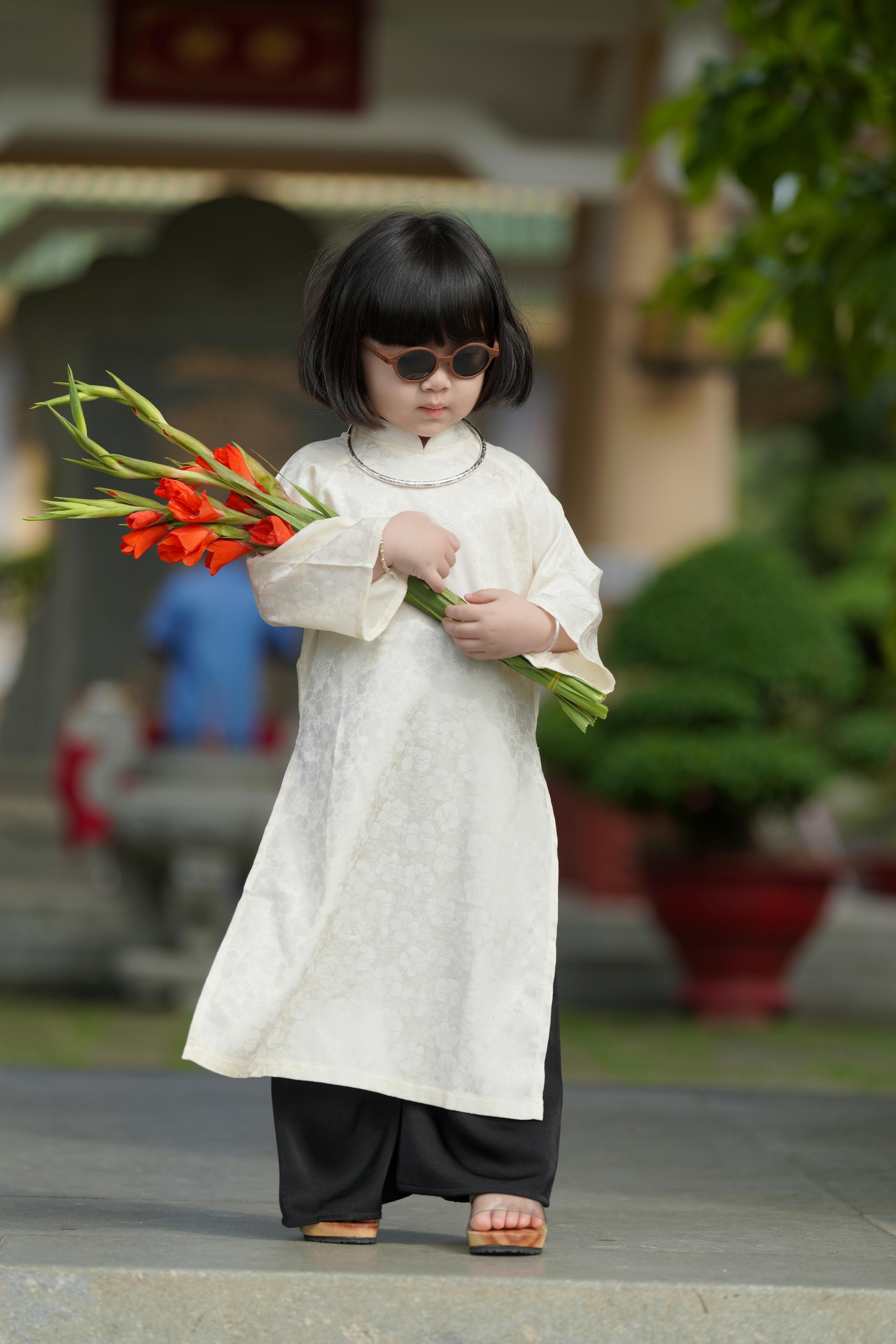 Young child with sunglasses holding flowers in a traditional outfit
