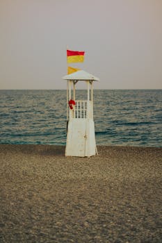 Lifeguard tower with red and yellow flag on a quiet pebble beach at dusk.