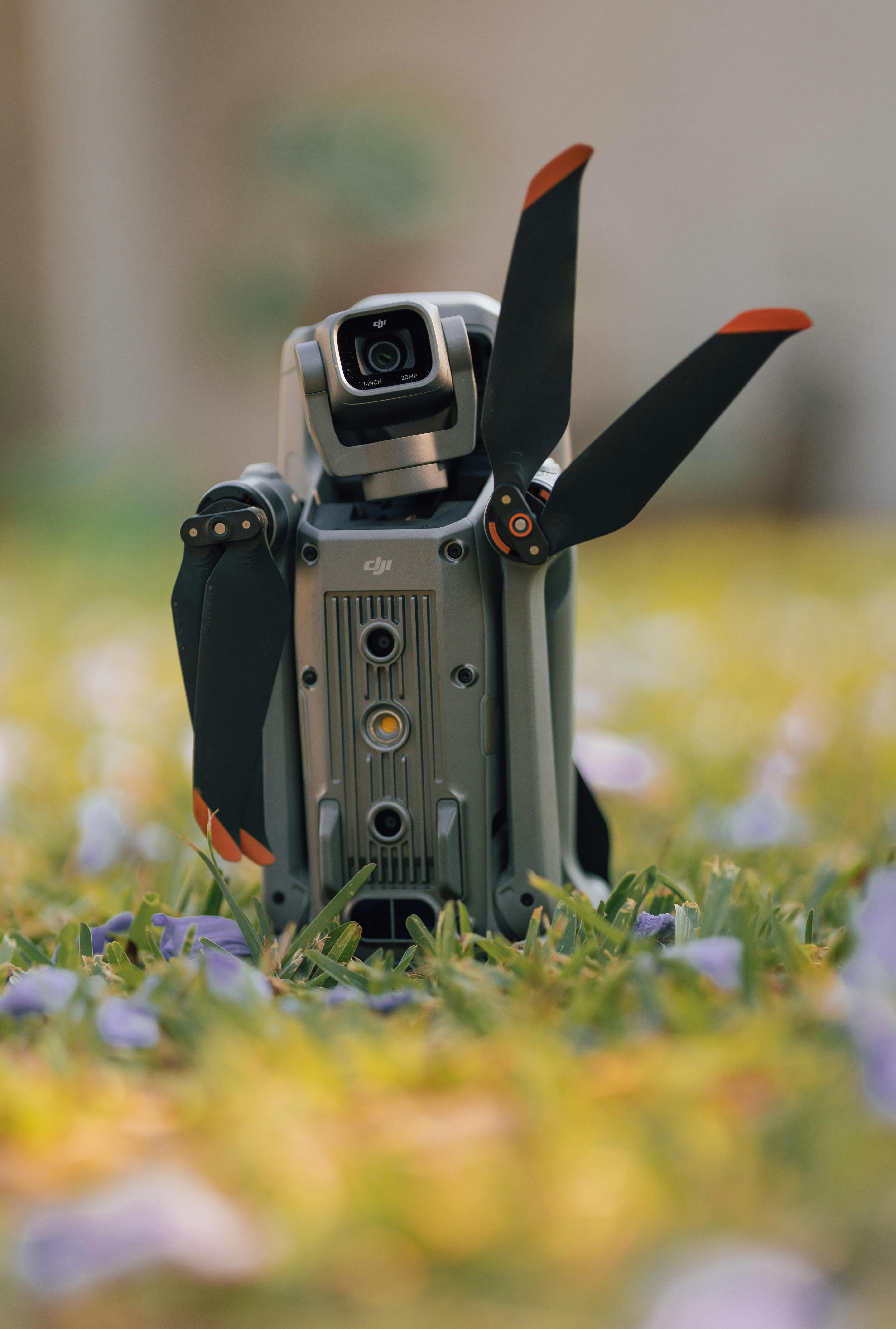 Free A portable drone resting on a grassy field with flowers, ready for takeoff. Stock Photo