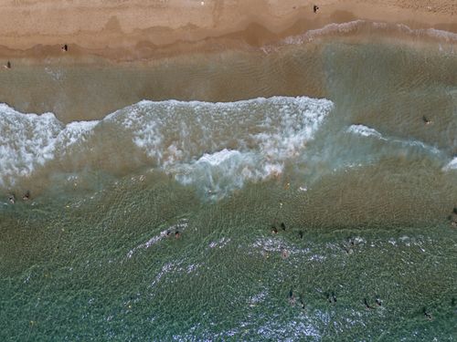 Free Aerial shot of Glyfada Beach in Greece showcasing azure waves crashing on the sandy shore. Stock Photo
