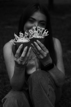 Woman holding birthday cupcakes with lit candles in artistic monochrome.