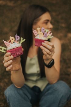 Woman holding two cupcakes with 'Happy Birthday' candles, celebrating outdoors.