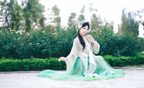 Woman in green traditional dress sitting in a park surrounded by lush greenery.