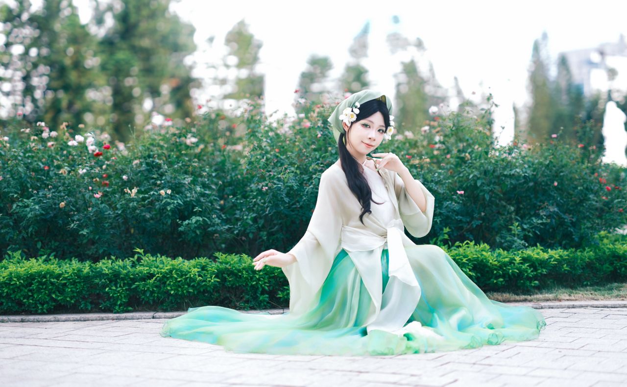 woman in green traditional dress sitting in a park surrounded by lush