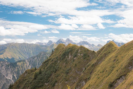 Aerial view of lush green mountains under a bright blue sky with clouds.