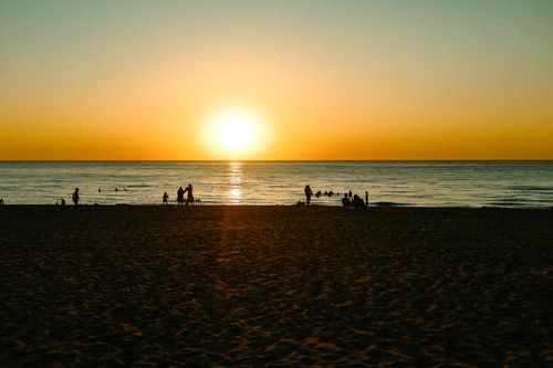 Free Silhouetted people enjoying a serene sunset on the beach, creating a tranquil summer scene. Stock Photo