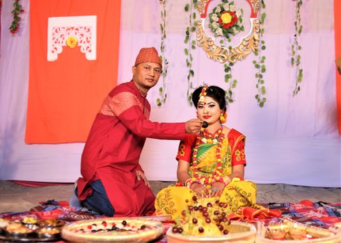 A couple in traditional attire partakes in a vibrant wedding ritual in Bangladesh.