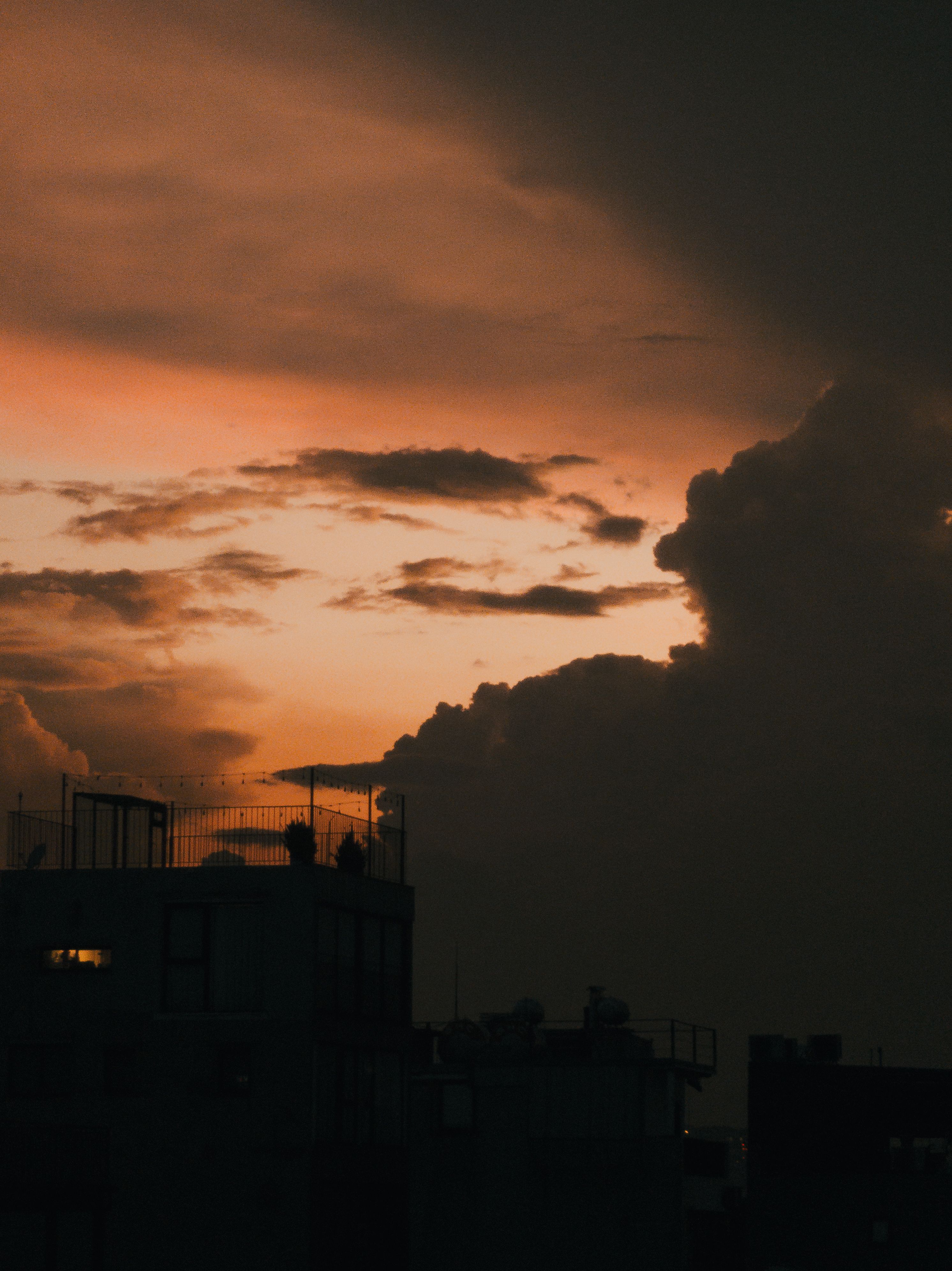 anime illustration of a Japanese school rooftop in golden sunset with orange clouds and a distant city