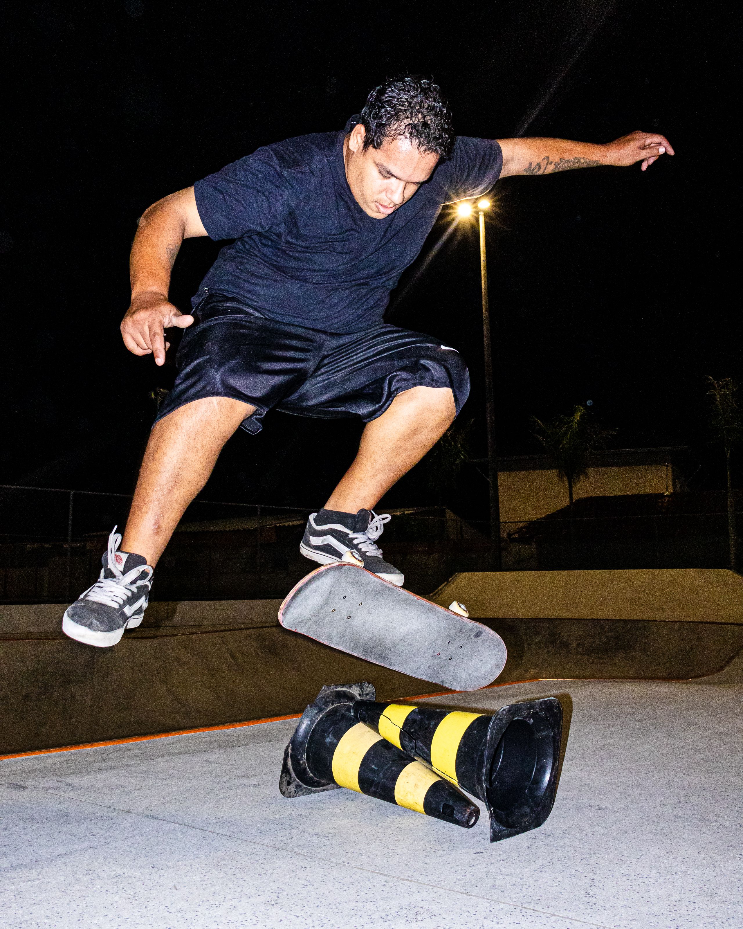 Skateboarder performs a trick mid-air over cones at a skate park during nighttime.. pexels, skateboarder, performs