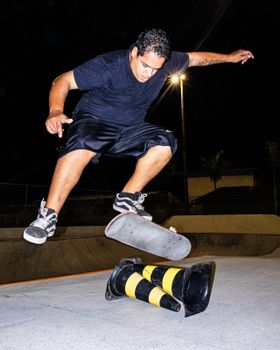Skateboarder performs a trick mid-air over cones at a skate park during nighttime.. pexels, skateboarder, performs
