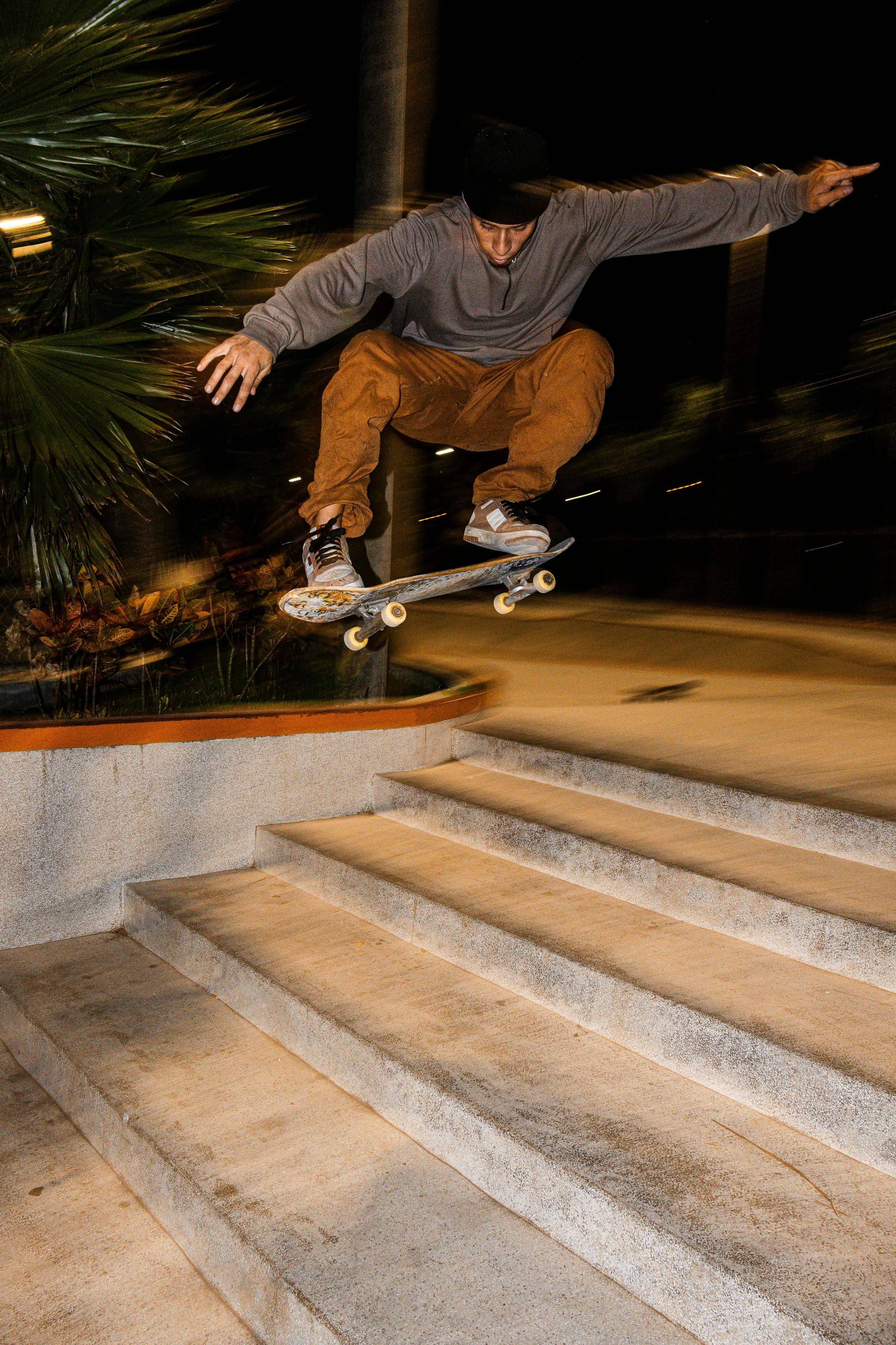 Skilled skateboarder executes an ollie over concrete stairs outdoors at night.