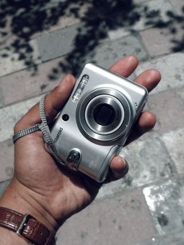 A hand holding a vintage Polaroid camera outdoors on a sunny day.