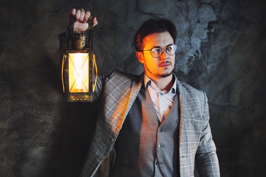 A man in a checkered suit holds a lantern casting warm light against a dark textured wall.