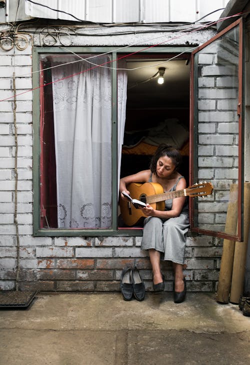 茶色のギターを保持しながら窓に座っている女性