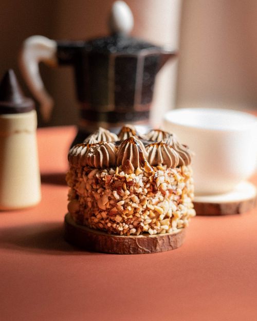 Free Close-up of a hazelnut cake with coffee pot and cup on a warm table setting. Stock Photo