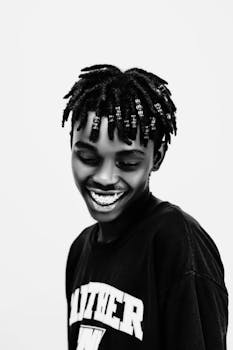 Dynamic black and white portrait of a young man smiling with distinctive hairstyle.