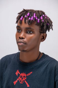 Stylish portrait of a young man with purple beaded hair on a neutral background.