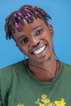 Vibrant portrait of a joyful man with colorful beaded dreadlocks and braces.