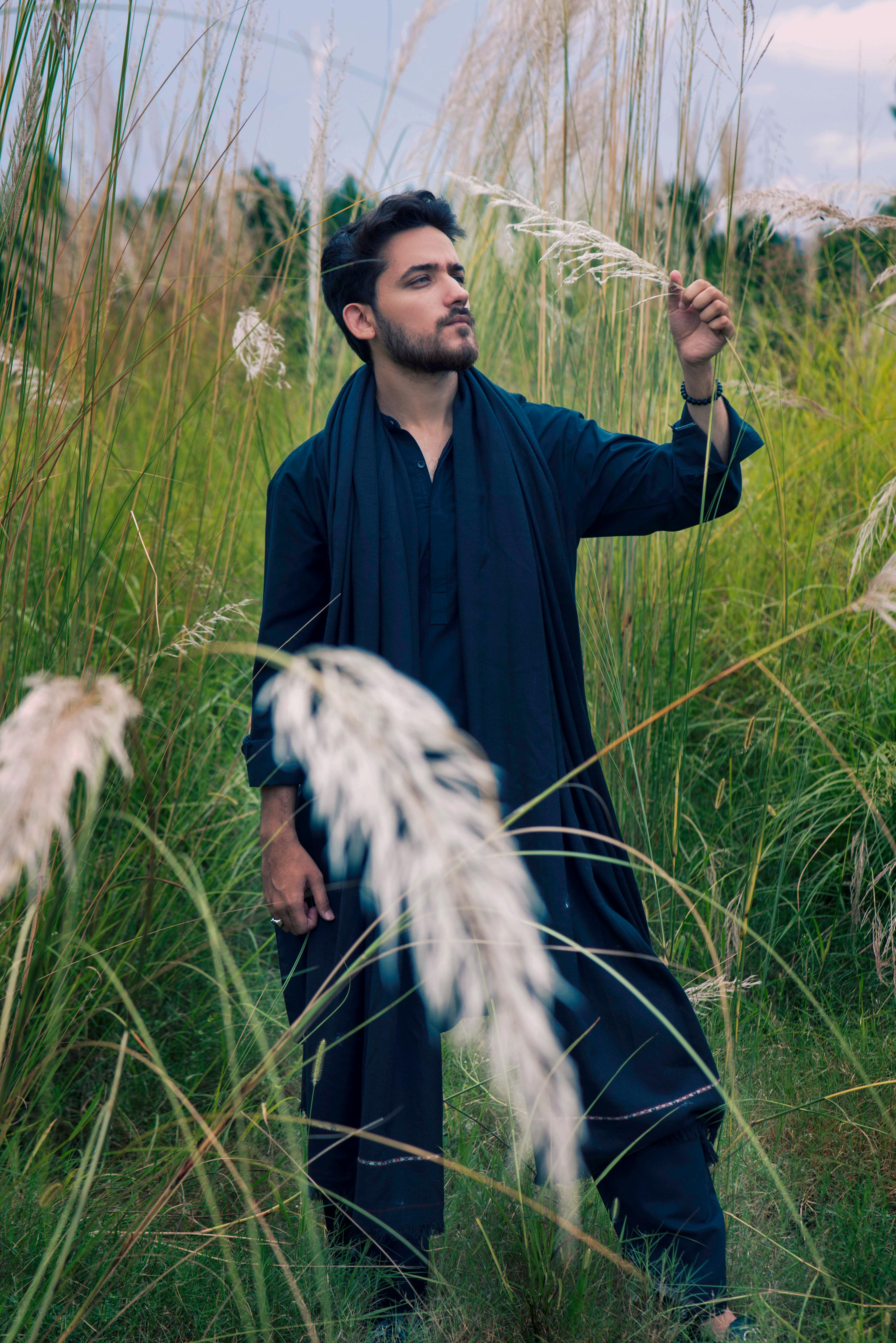 bezplatná Muž v tradičním oděvu stojí venku uprostřed vysoké trávy a evokuje klidnou a kontemplativní náladu. Základová fotografie