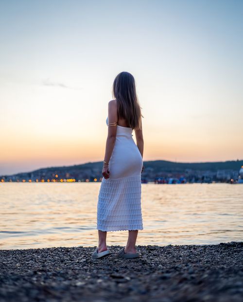 Free Young woman admires sunset by the sea in Vodice, Croatia, wearing a white dress. Stock Photo