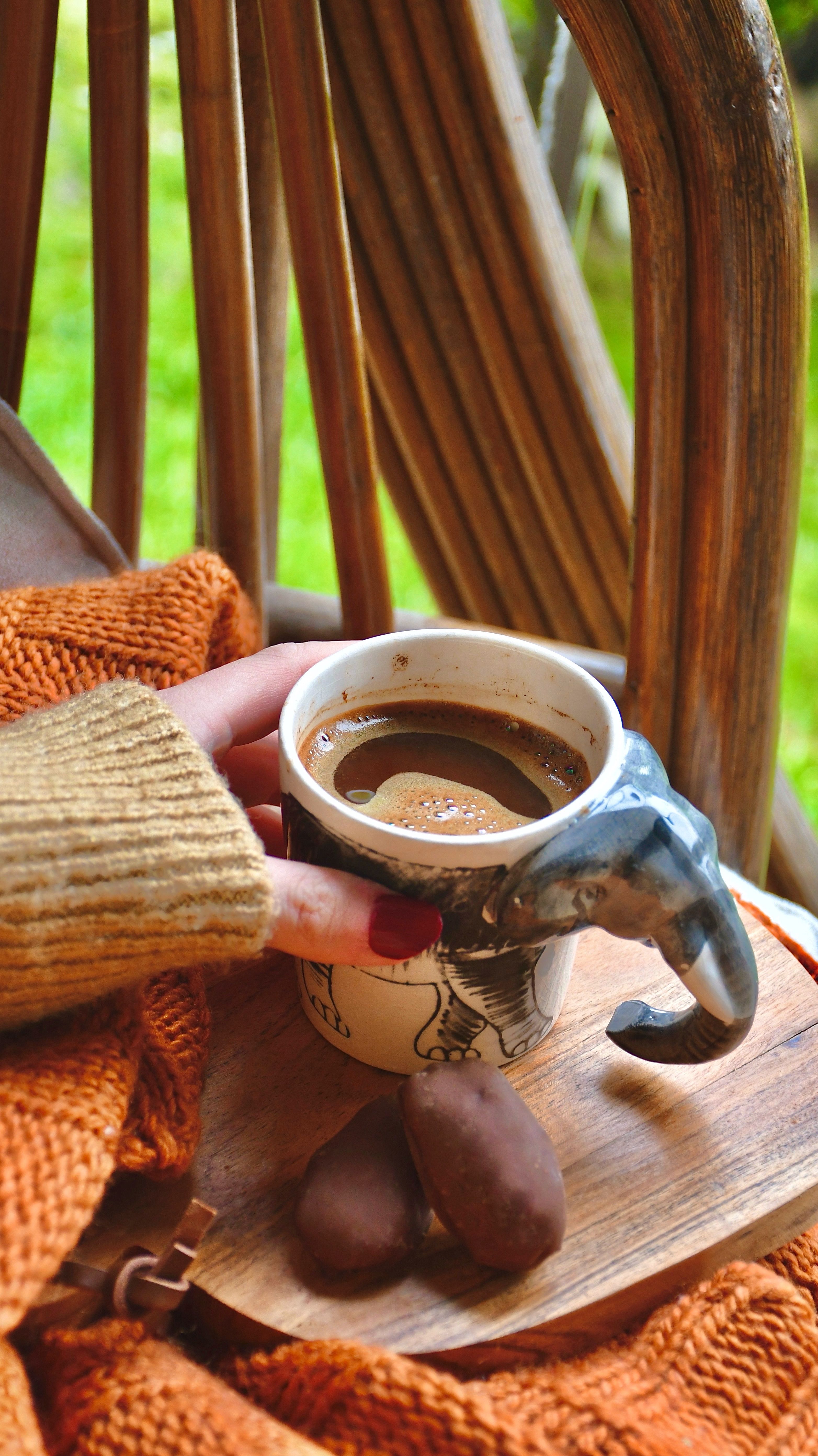 Hand holding elephant-shaped cup with coffee on a cozy autumn day outdoors.