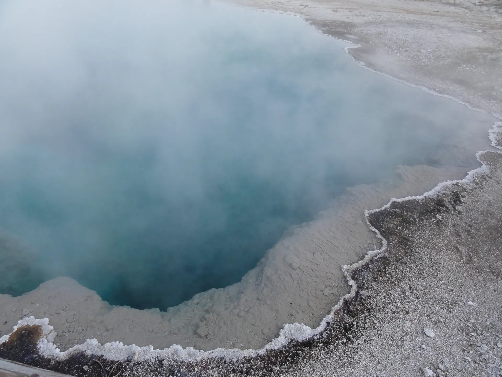 Steaming hot spring in Yellowstone National Park with a blue pool surrounded by mineral deposits. Steaming hot spring in Yellowstone National Park with a blue pool surrounded by mineral deposits.