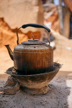 A vintage iron kettle rests on a traditional outdoor stove in a rustic setting.