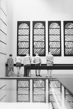 Visitors admire artwork in a modern museum, reflected elegantly on surfaces.