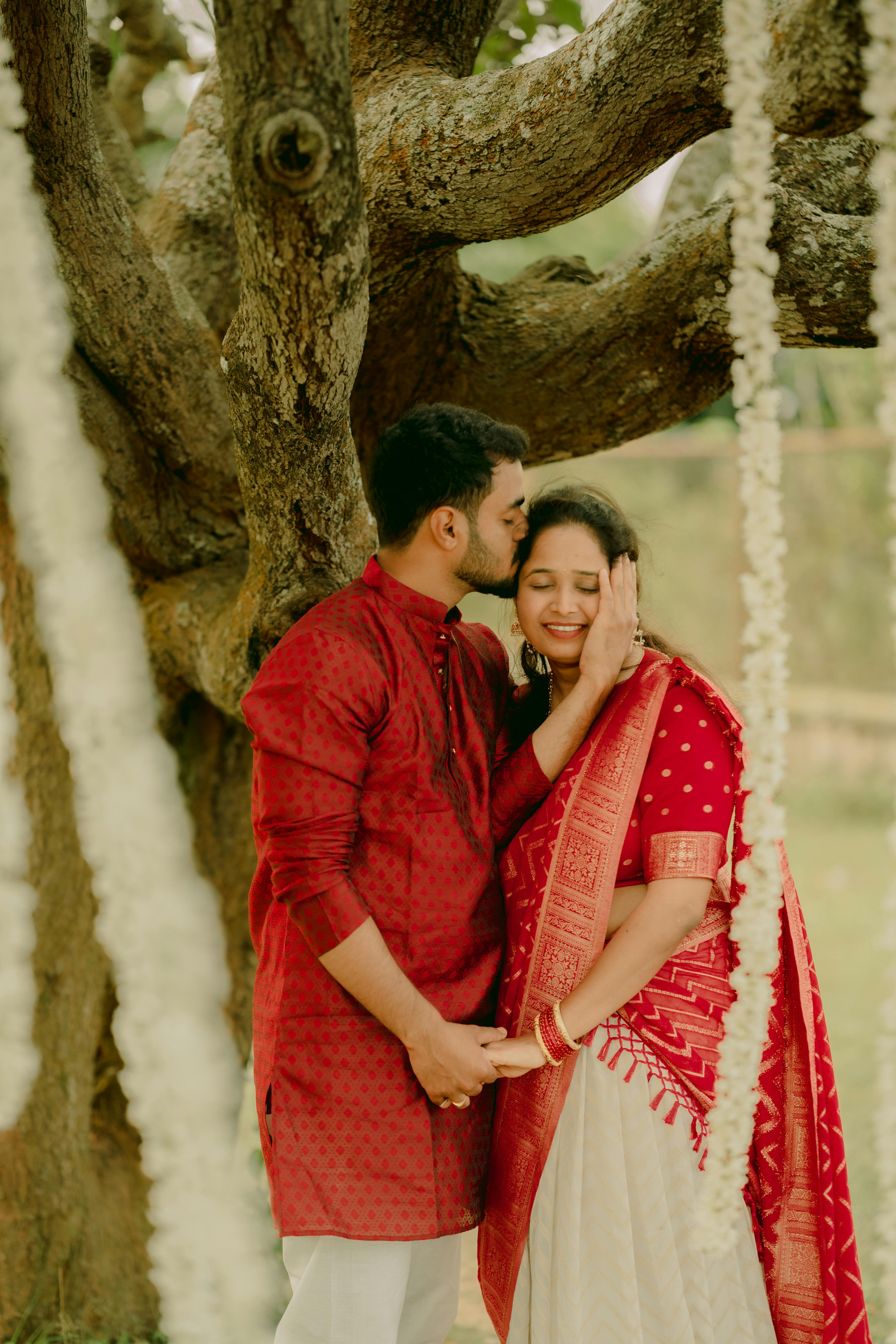 A couple shares a tender moment under a tree adorned with flowers, celebrating love and togetherness.