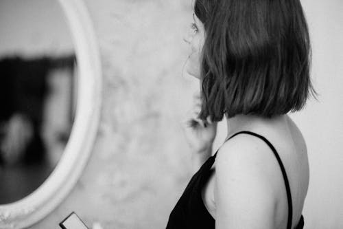 Grayscale Photo of Woman Standing in Front of Mirror