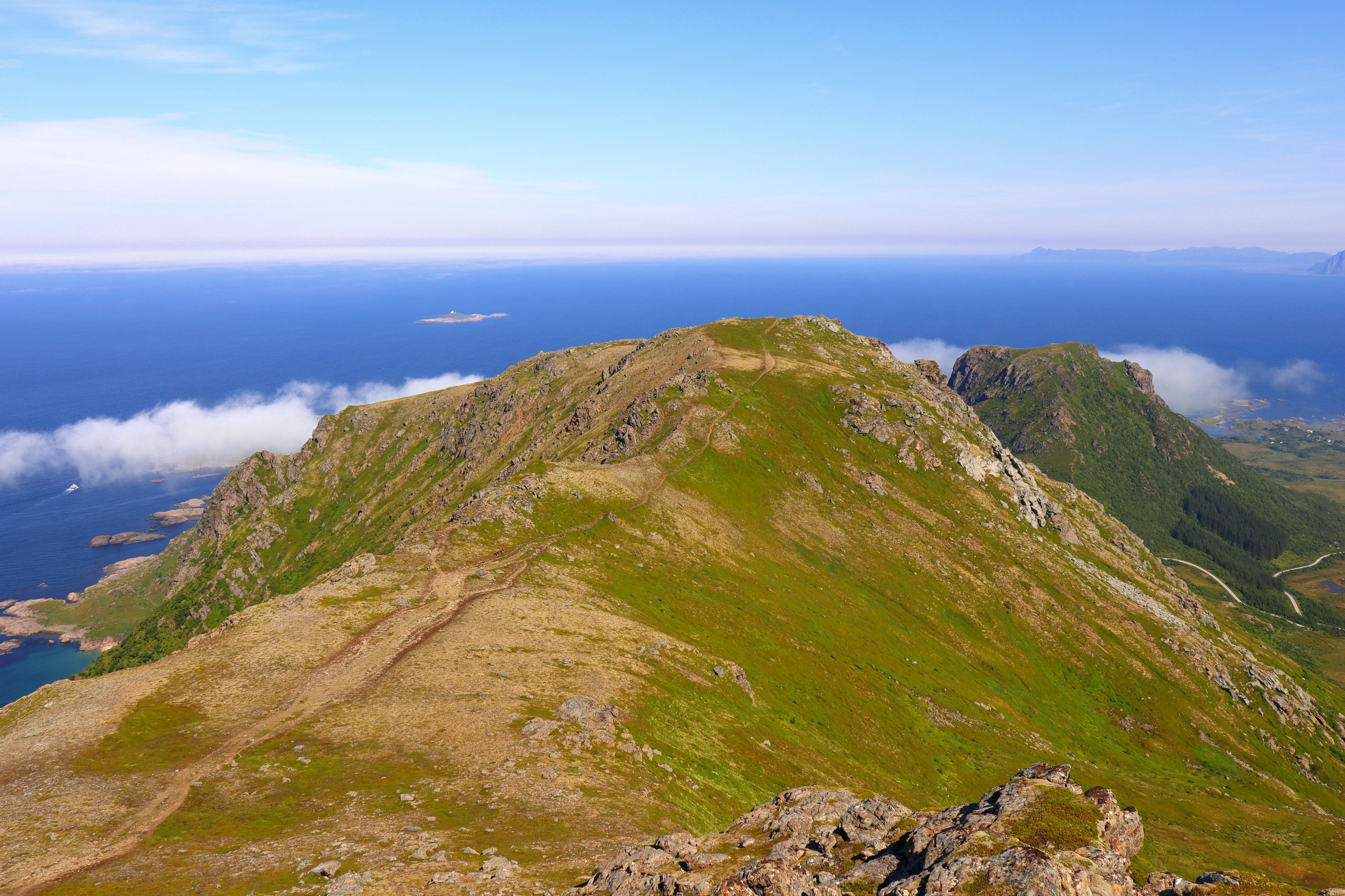 Gratis En fantastisk utsikt over fjell og hav med klar himmel og frodig grøntområde. Arkivbilde
