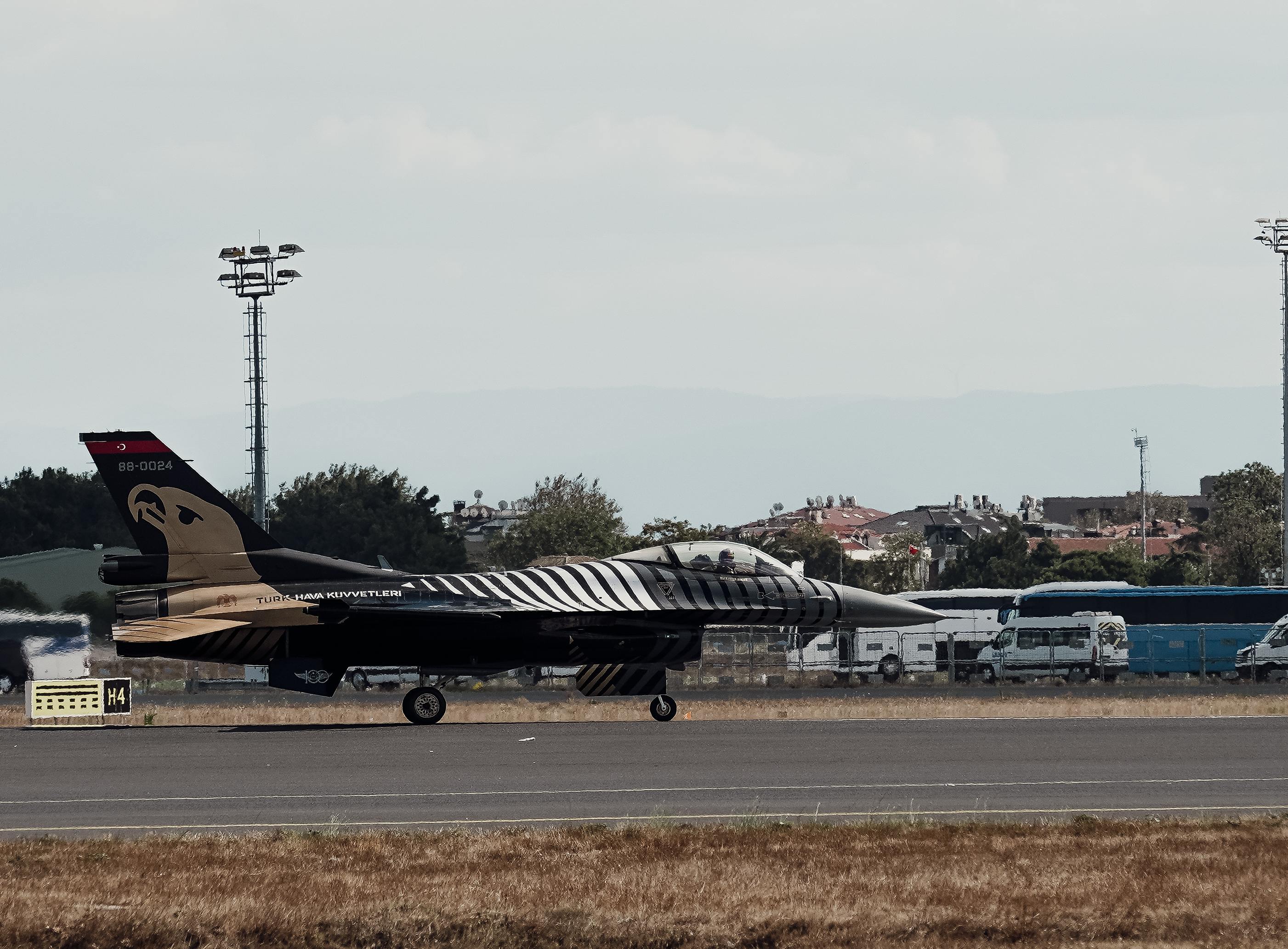 A military jet with a unique paint job taxies on an airfield runway.