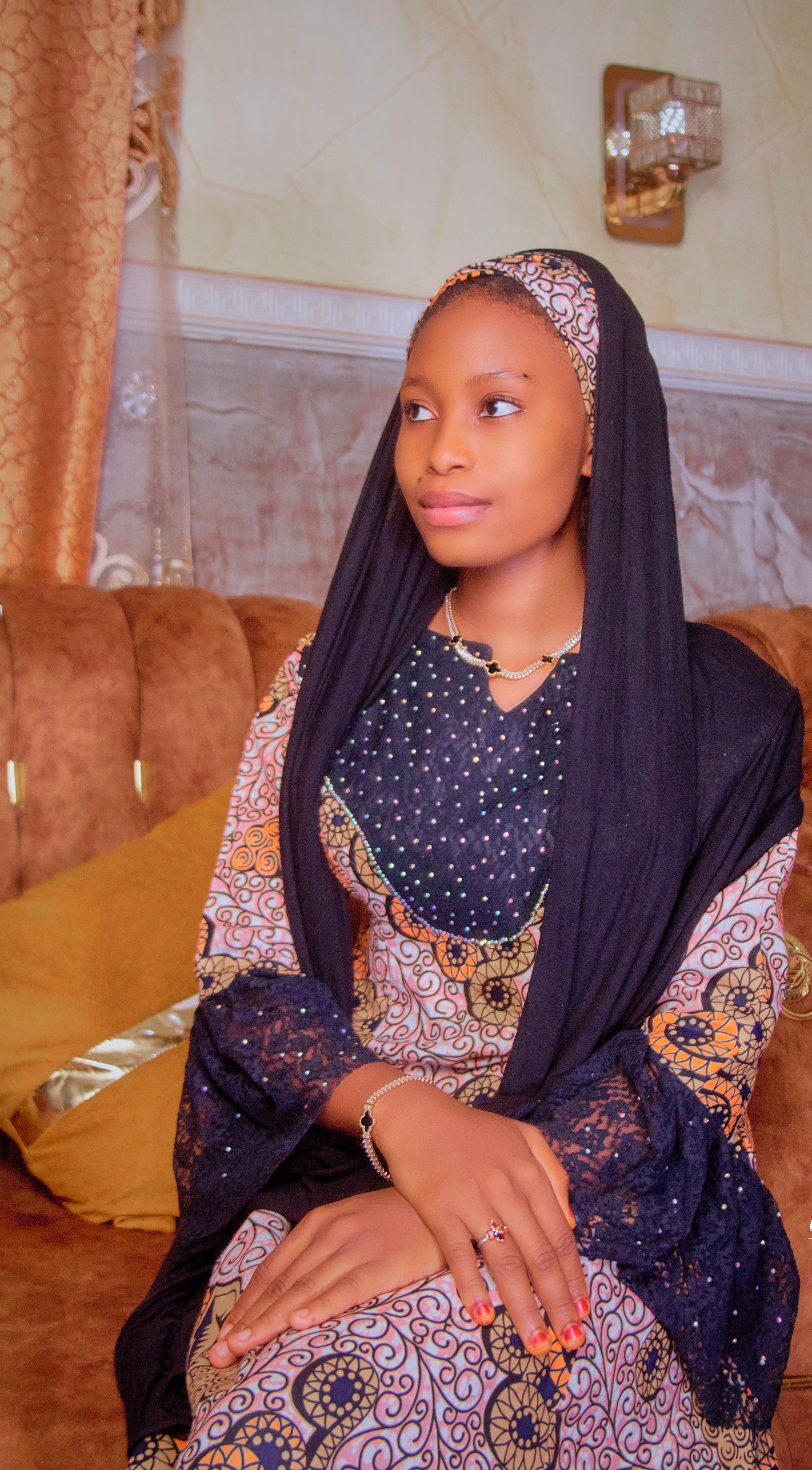 A young woman in traditional clothing is seated indoors, exuding elegance and grace.