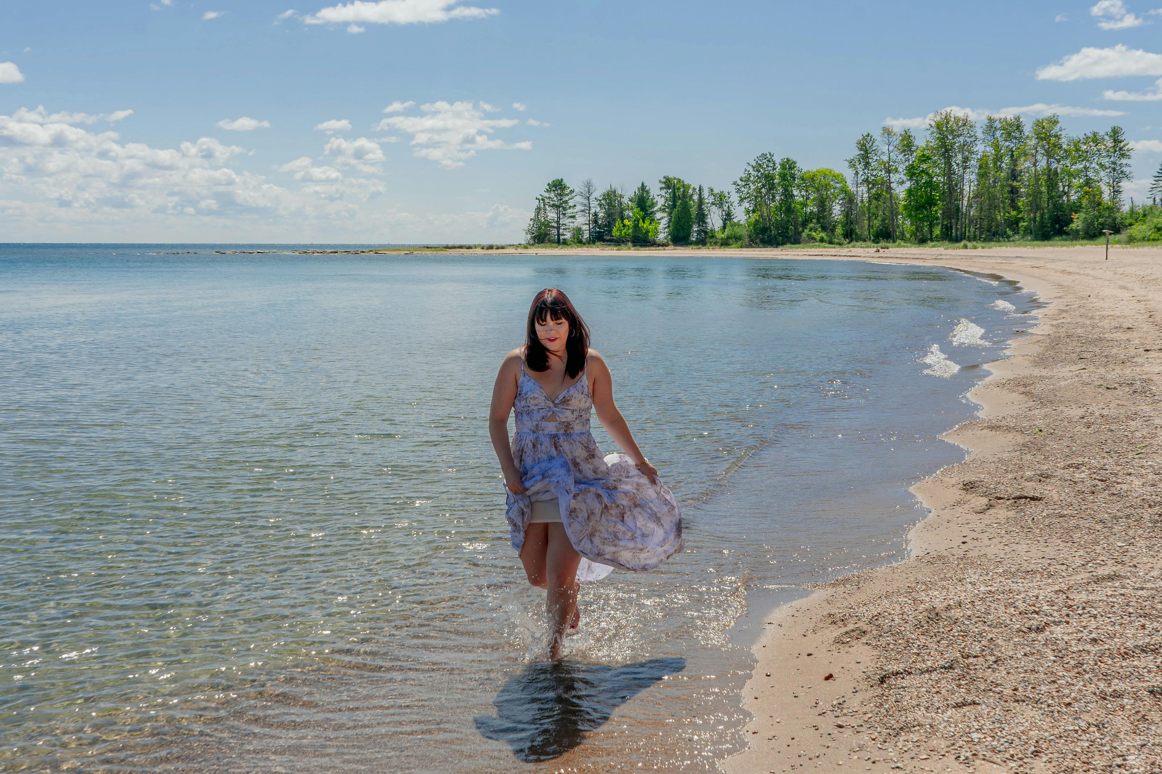 A stylish woman in a summer dress splashes along the shore of Sturgeon Bay, Wisconsin. Perfect for fashion and travel themes.