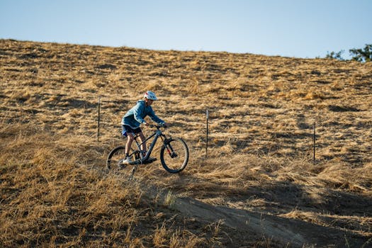 Teenage boy mountain biking on a dry hillside in summer sun.