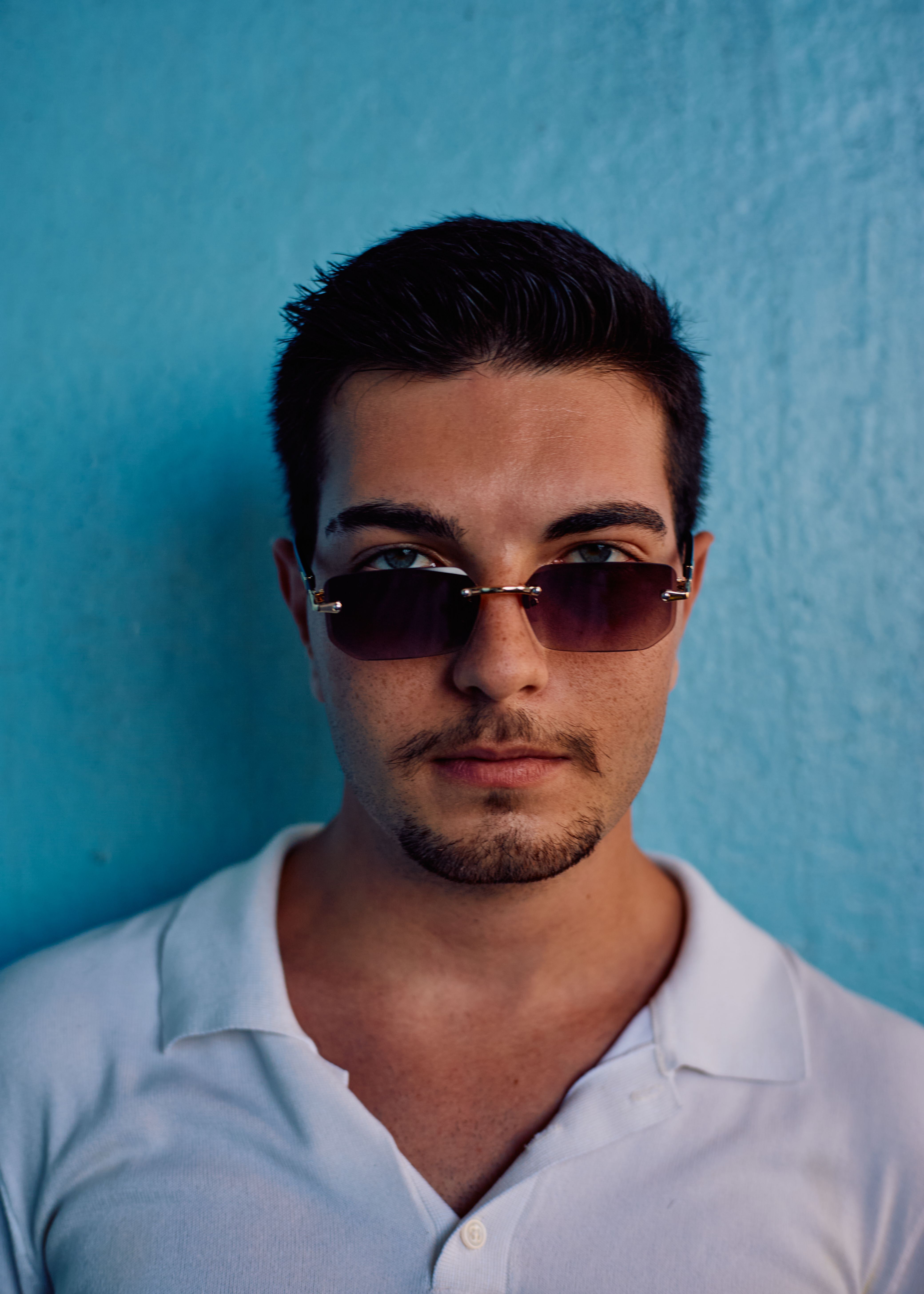 Stylish portrait of a young man in sunglasses against a teal wall in Istanbul, Turkey.