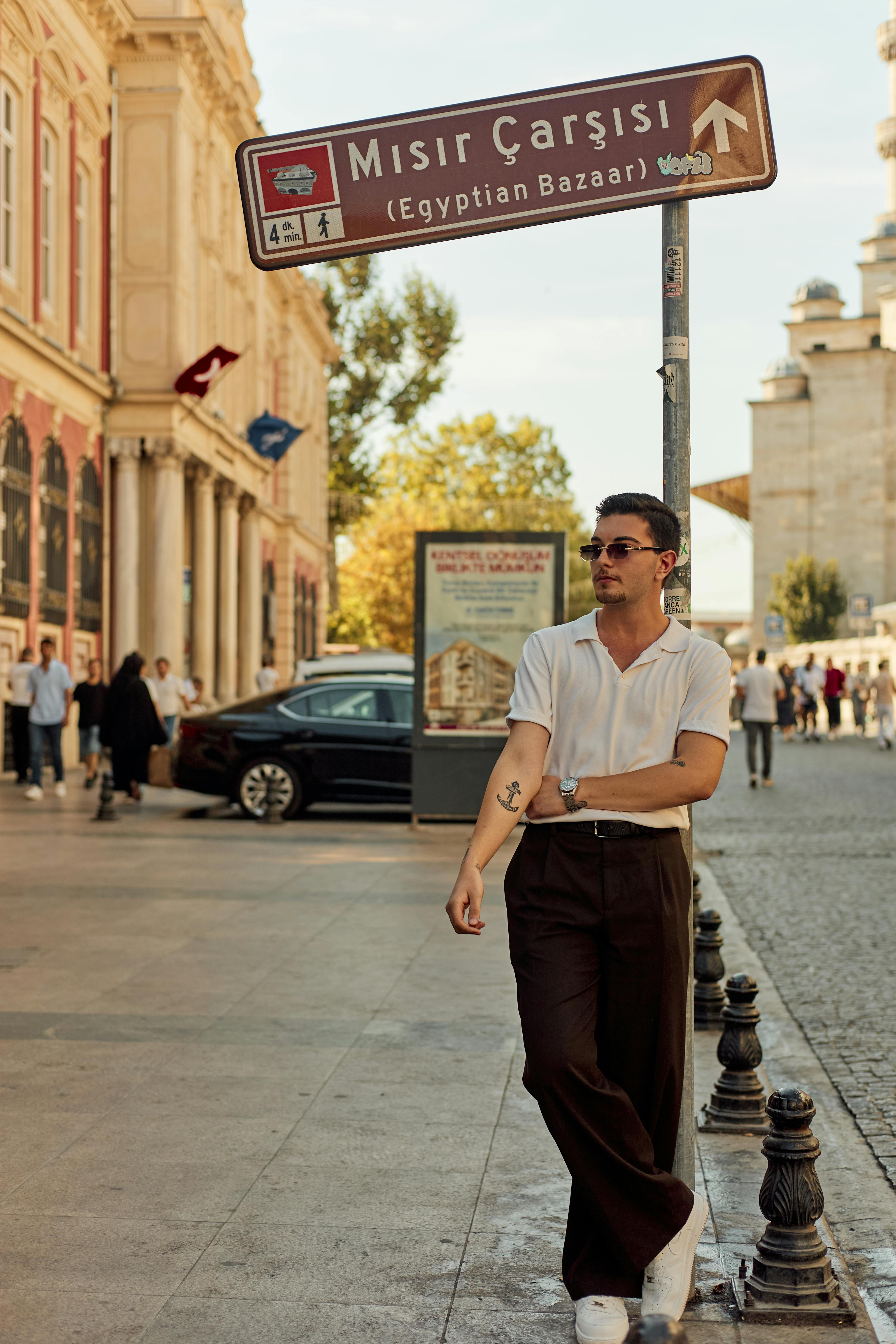 Stylish man leaning against a sign for Istanbul's famous Egyptian Bazaar on a sunny day.